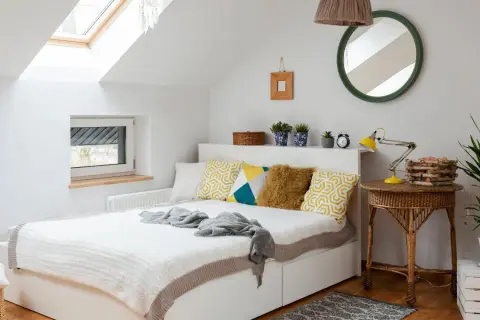 Chambre sous pente lumineuse avec lit blanc, coussins géométriques, et un puits de lumière. Une belle idée peinture pour un espace cosy.