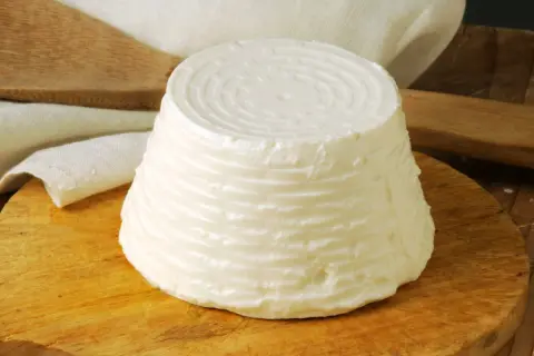 Świeży serek ricotta o stożkowatym kształcie, z charakterystycznym wzorem na wierzchu, leży na drewnianej desce.