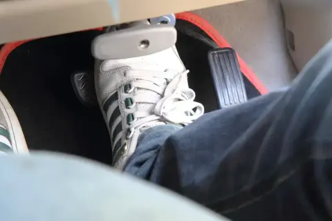 Pédale de frein enfoncée, signe d'un symptôme de mauvaise purge frein. La chaussure blanche et jean bleu sont visibles.