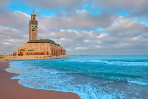 Wspaniałe maroko wakacje! Meczet Hassana II w Casablance nad turkusowym oceanem, z piaszczystą plażą i chmurami na niebie.