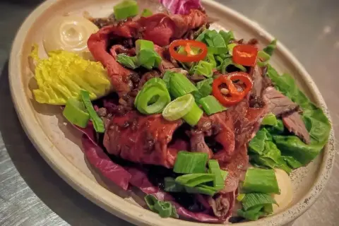 En läcker sallad med marinerad rostbiff, garnerad med salladslök och chili. Serveras med en krämig sås och krispig sallad.
