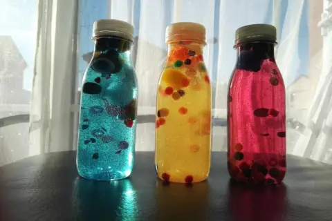 Tres botellas sensoriales caseras llenas de líquido brillante y bolitas de colores.