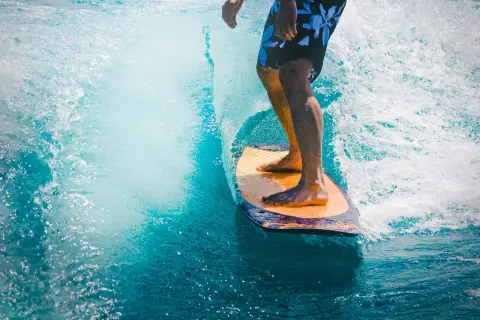 Mężczyzna na desce surfingowej, czując orzeźwienie wody, jak po użyciu perfum allure homme sport.