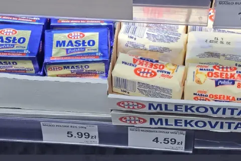Na półce sklepowej widać opakowania masła. Jedno z nich, "Masło Polskie 82%", waży 100 gramów. Obok leżą mniejsze kostki masła "Osełka Mini" również po 100 gramów.