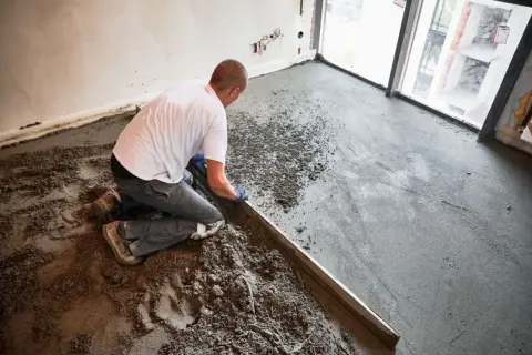 Budowlaniec wyrównuje świeżą wylewkę anhydrytową na podłodze, używając łaty.