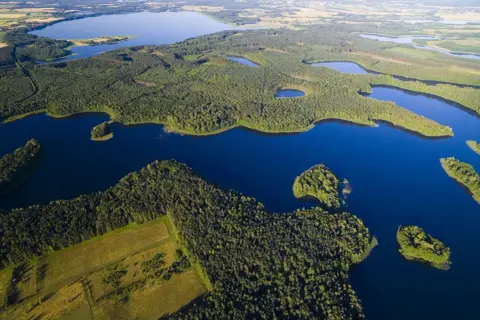 Malowniczy krajobraz z lotu ptaka: rozległe, ciemnoniebieskie jeziora otoczone gęstymi lasami i zielonymi polami. Prawdziwa kraina wielkich jezior.