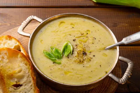 Una ciotola di calda crema di patate, guarnita con cipollotto fresco e pepe nero, servita con fette di pane tostato.