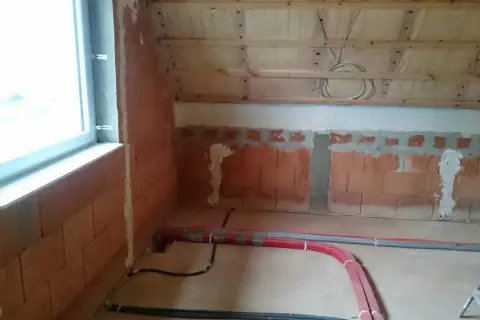 Neue Heizungsrohre verlegen im Rohbau. Rote und graue Rohre liegen auf dem Boden, bereit für die Installation.