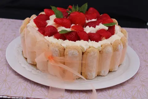 Charlotte aux fraises et fromage blanc, décorée de crème fouettée et de menthe fraîche. Un ruban pêche enlace le pourtour de biscuits à la cuillère.
