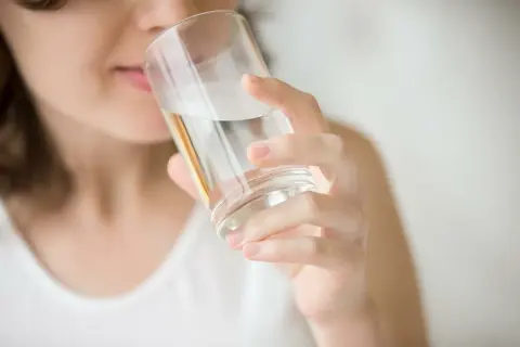 Kobieta pije wodę z filtra, która ma gorzki smak.