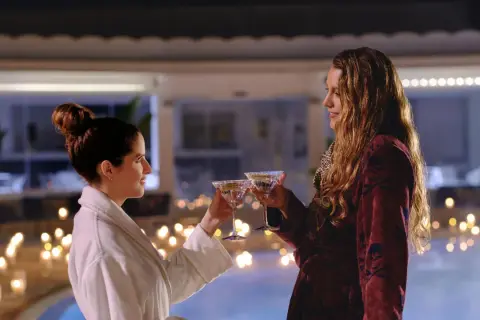 Zwei Frauen stoßen mit Martinis an, umgeben von Kerzenlicht und einem Pool. Nur noch ein kleiner gefallen, bevor der Abend perfekt ist.