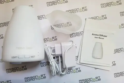Un diffuseur d'arômes blanc, son adaptateur et son manuel. Un objet connecté pour une ambiance olfactive personnalisée.