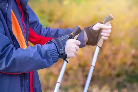 Osoba w kurtce przygotowuje się do marszu, trzymając kijki trekkingowe. Poznaj, jak chodzić z kijkami trekkingowymi, by czerpać z tego maksimum korzyści.
