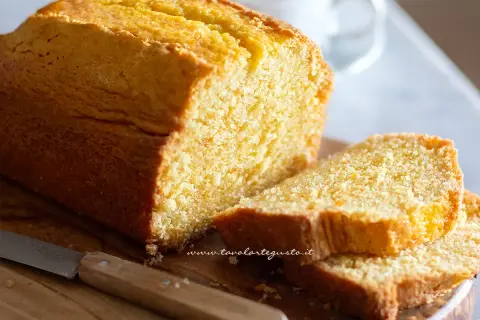 Plumcake senza yogurt dorato e soffice, tagliato a fette su un tagliere di legno con un coltello.