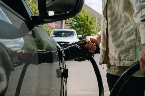 Persona che collega il cavo di ricarica a un'auto elettrica, un'azione che influisce sul costo ricarica auto elettrica.