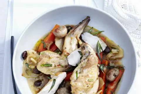 Ein köstliches Gericht mit zartem wirsing kaninchen, Karotten, Oliven und Kräutern in einer aromatischen Sauce, serviert in einer weißen Schüssel.