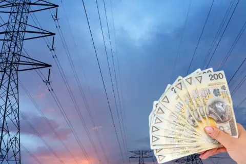 Dłoń trzyma banknoty 200 zł na tle linii energetycznych. Zastanawiasz się, ile kosztuje 1 kWh PGE?