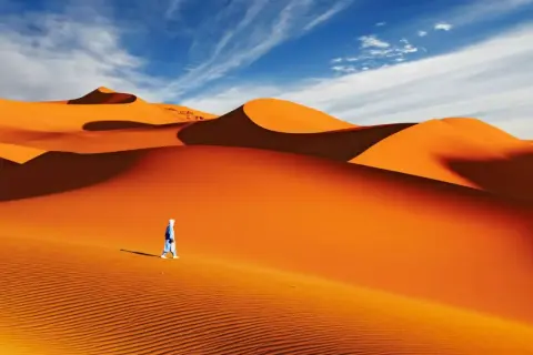Un voyageur solitaire traverse la majestueuse dune du Sahara sous un ciel bleu éclatant.
