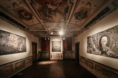 Sala di una galleria d'arte con soffitto affrescato e opere moderne. Le mostre ad Ancona presentano un'installazione con un volto stilizzato e un'opera astratta.