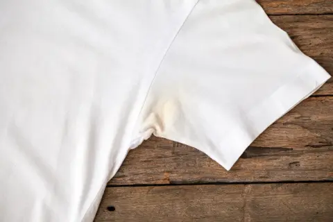 Verkrustete Deoflecken entfernen: Ein weißes T-Shirt mit gelblichen Flecken unter dem Arm auf Holzuntergrund.