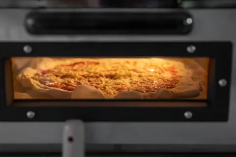 Ein Pizzateig, der 24 Stunden gereift ist, wird in einem Ofen gebacken. Er ist mit Tomatensauce und Käse belegt und verströmt einen köstlichen Duft.