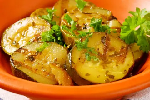 Gegrillte Schmorgurken mit Speck, garniert mit Petersilie, in einer orangen Schale.