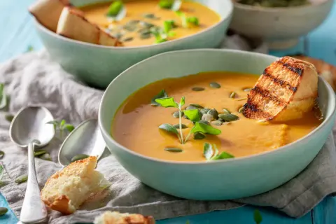Zwei Schalen cremiger Kürbissuppe mit geröstetem Brot und Kürbiskernen. Perfekt für leichte Schonungskost-Rezepte.