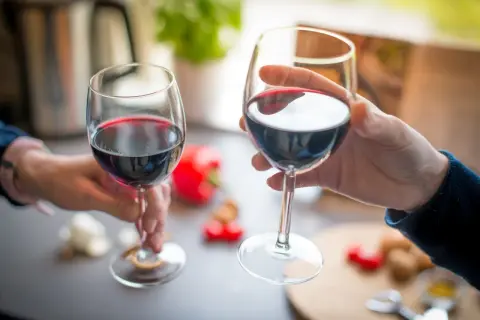 Dwie dłonie unoszą kieliszki z czerwonym winem, celebrując chwilę. Idealny sposób, jak pić wino.