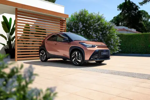 Różowy Toyota Aygo X na podjeździe przed nowoczesnym domem. Sprawdź atrakcyjną toyota aygo x cena!