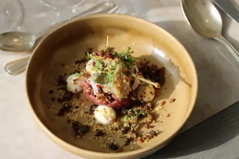 En konstnärlig råbiff med kapris, ägg och örter, serverad i en rustik skål. En kulinarisk upplevelse från Fjelie vingård.