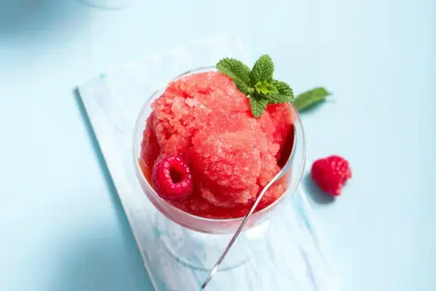Erfrischendes Himbeer-Slush-Eis selber machen: Ein Glas gefüllt mit leuchtend rotem Slush-Eis, garniert mit frischen Himbeeren und Minze.