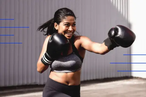 A woman in a boxing blade stance throws a punch, smiling.