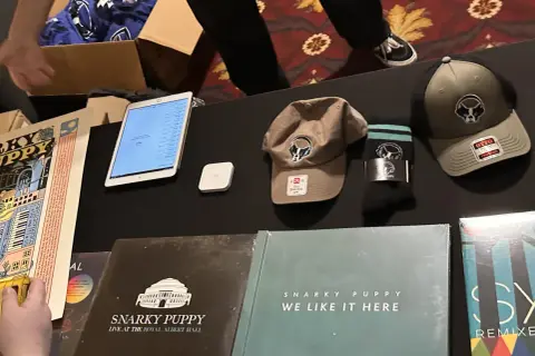 Snarky Puppy merchandise: vinyl records, hats, socks, and a tablet displaying a setlist.