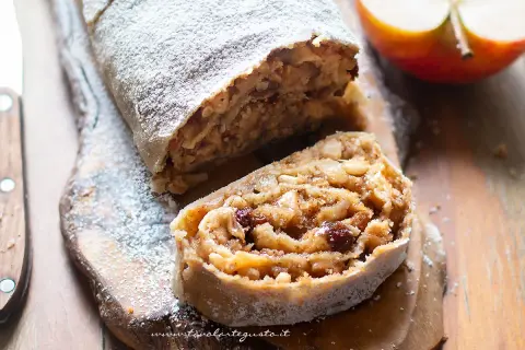 Strudel di mele con pasta sfoglia, cosparso di zucchero a velo, su tagliere di legno.