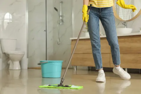 Nettoyer carrelage après chantier : une personne en gants jaunes passe la serpillière sur un sol brillant dans une salle de bain moderne.