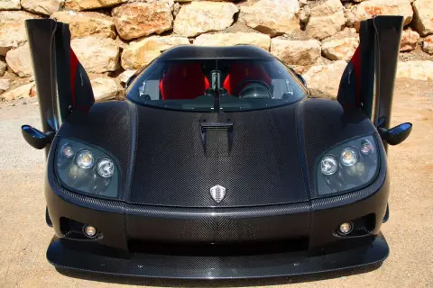 Czarny Pagani z otwartymi drzwiami, wykonany z włókna węglowego, z czerwonymi siedzeniami, na tle kamiennej ściany.