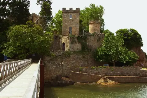 Un puente de madera conduce al histórico castillo de Santa Cruz, rodeado de exuberante vegetación y con vistas al mar.