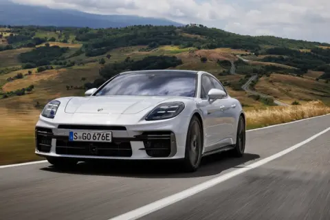Białe Porsche Panamera GTS sunie po krętej drodze wśród malowniczych wzgórz Toskanii.