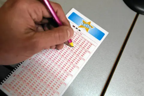 Dłoń z różowym ołówkiem zaznacza liczby na kuponie Lotto.
