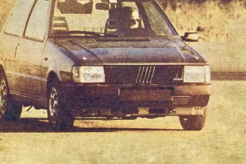 Ciemny Fiat Uno Turbo z kierowcą za kierownicą, gotowy do jazdy.
