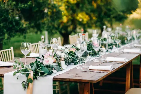 Tavola apparecchiata all'aperto con candele, fiori e bicchieri. Un esempio di addobbi tavoli matrimonio fai da te, con un tocco rustico ed elegante.