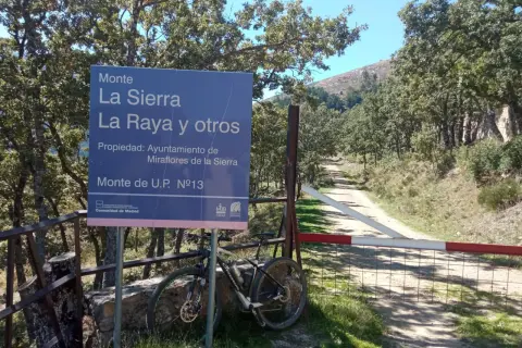 Señal de "Puerto de la Morcuera" junto a una bicicleta de montaña. Camino rural y árboles en un día soleado.