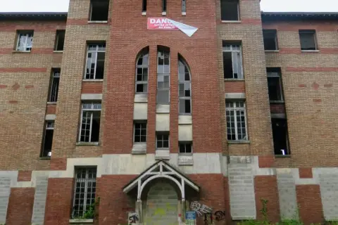 Façade imposante de l'hôpital abandonné d'Angicourt, avec ses fenêtres brisées et un panneau "DANGER ACCÈS INTERDIT AU PUBLIC".