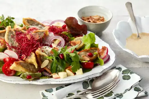 Herzhafter Maultaschen Salat mit knackigem Gemüse, roten Zwiebeln, Granatapfelkernen und Mandelsplittern. Dazu eine cremige Sauce.