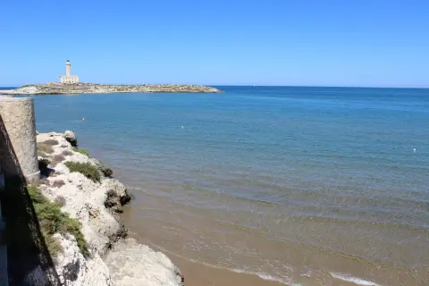 Faro di Vieste, Stella Maris, su un'isola rocciosa con mare azzurro e spiaggia sabbiosa.