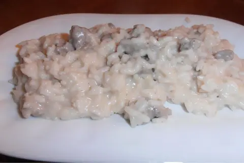 Un cremoso risotto salsiccia e patate, servito su un piatto bianco.