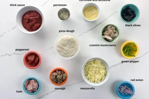 Pinsa z czym zrobić? Składniki: sos, parmezan, ciasto, pepperoni, szynka, kiełbaska, mozzarella, kukurydza, oliwki, pieczarki, papryka, cebula.