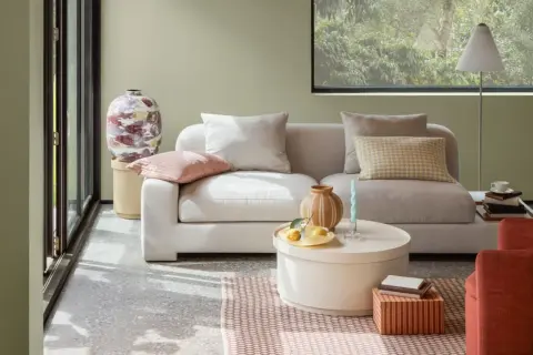 Gemütliches Wohnzimmer mit hellgrauem Sofa, Kissen in sanften sommer farben und einem runden Couchtisch.