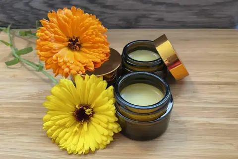 Zwei Gläser mit selbstgemachter Ringelblumensalbe, daneben leuchtend orange und gelbe Ringelblumen.