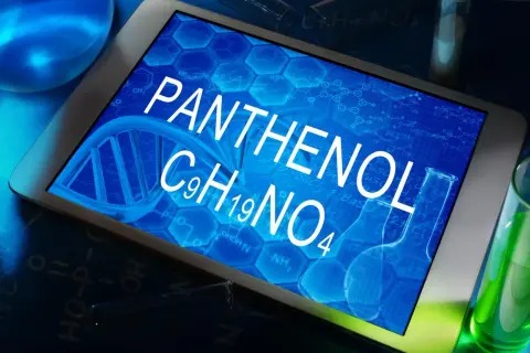 Tablet z napisem PANTHENOL i wzorem chemicznym C9H19NO4, otoczony probówkami z zielonym płynem i elementami chemicznymi.